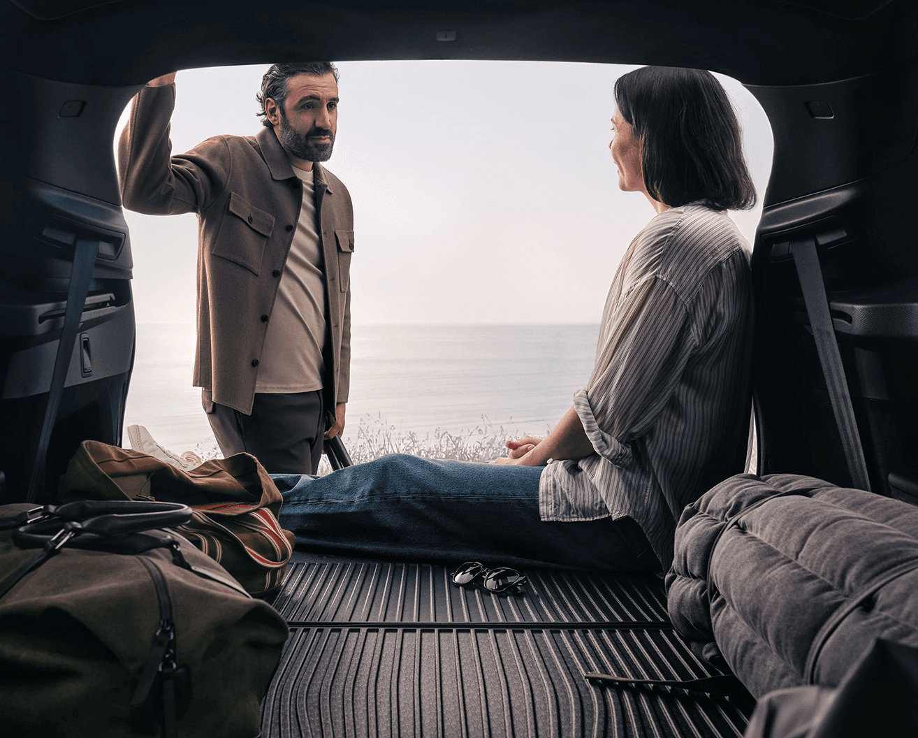 Casal guardando bagagens no porta-malas de um Volvo com vista para o mar